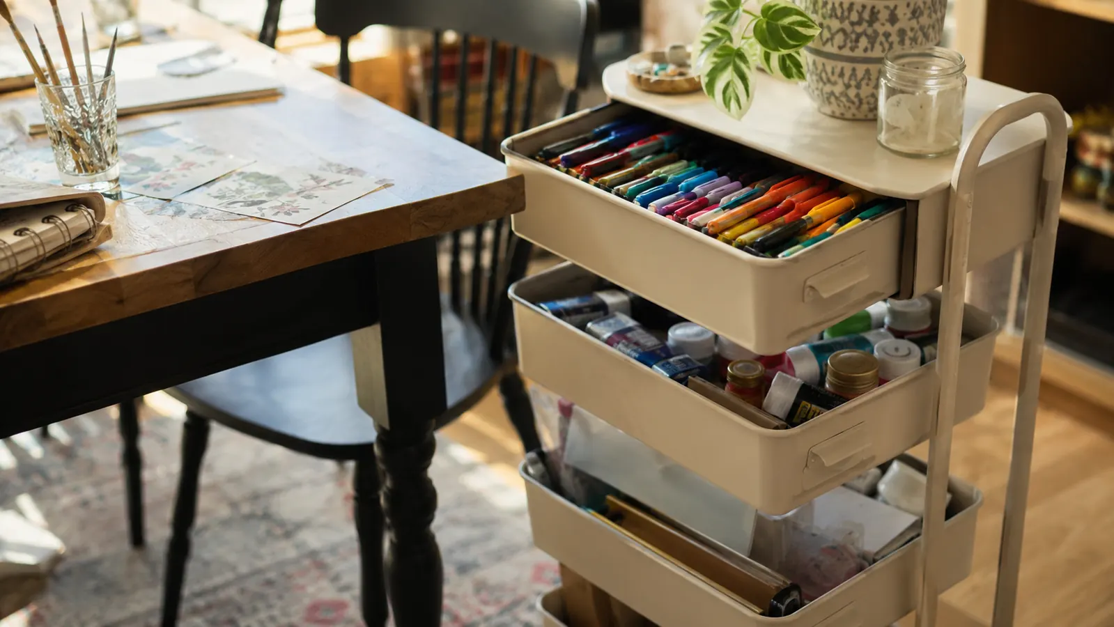 Rolling cart serving as a mobile craft station next to a table with art supplies organized in each drawer