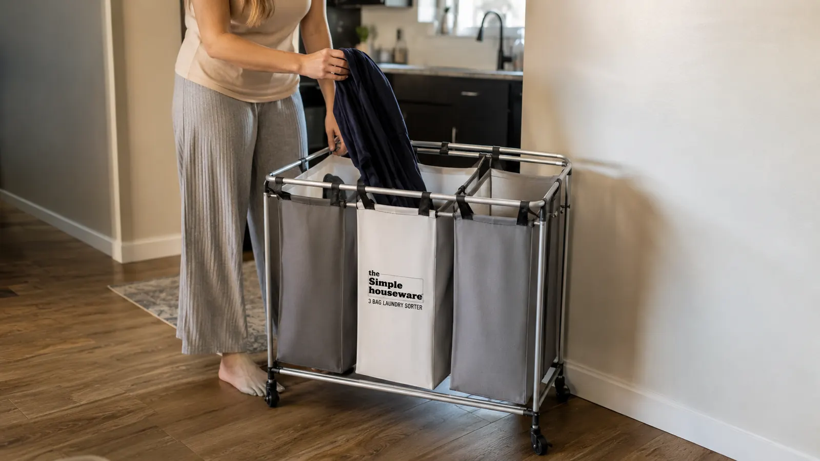 A woman dropping a dark shirt directly into the correct bag on a rolling laundry sorter without bending down