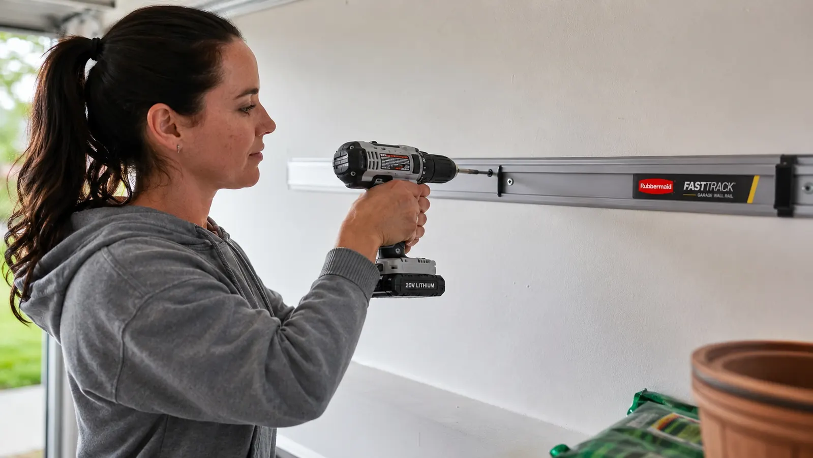 Woman mounting a FastTrack rail to a garage wall with a power drill