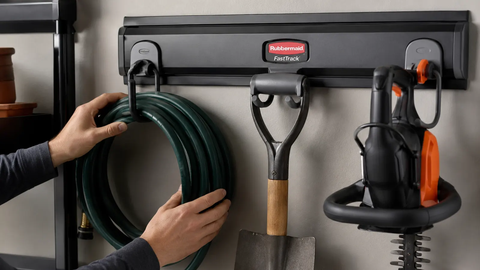 Close-up of FastTrack hooks holding a garden hose, shovel, and hedge trimmer on a rail