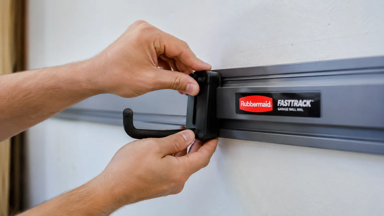 Close-up of a hand sliding a Rubbermaid FastTrack hook onto a wall-mounted rail in a garage