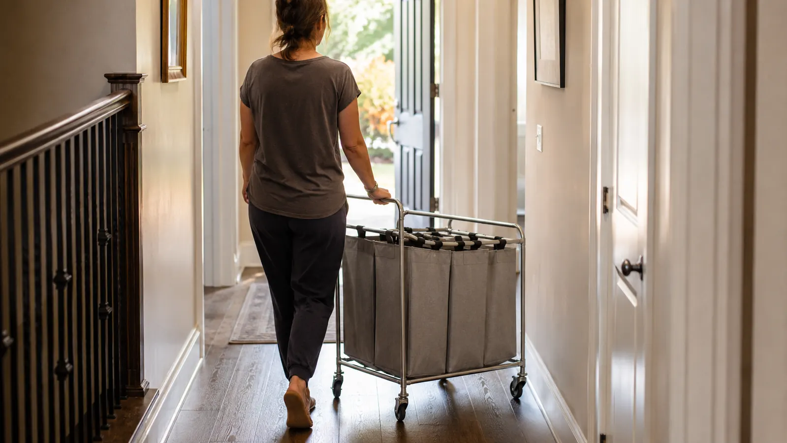 Woman rolling the Simple Houseware laundry sorter across a hallway toward a laundry room door, cart lightly loaded